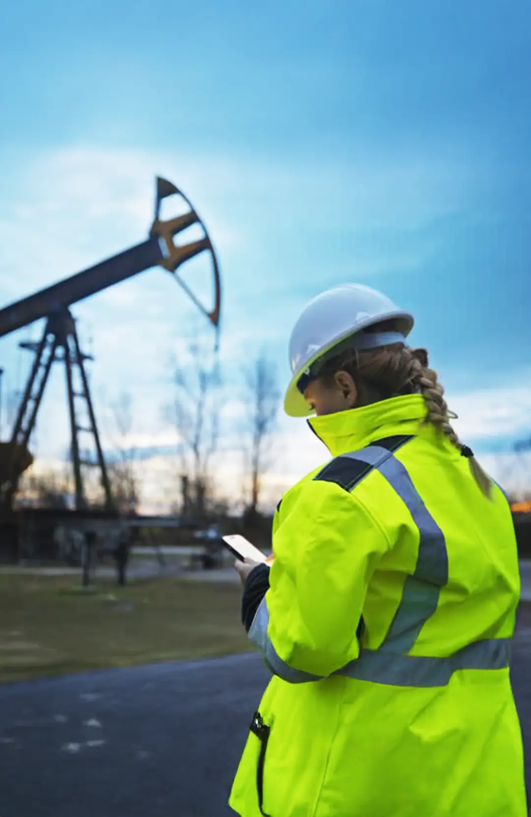 Woman using her phone in front of an oil jack